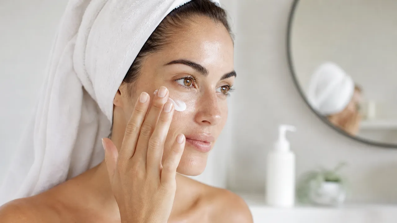 Femme appliquant une crème hydratante sur son visage devant un miroir de salle de bain